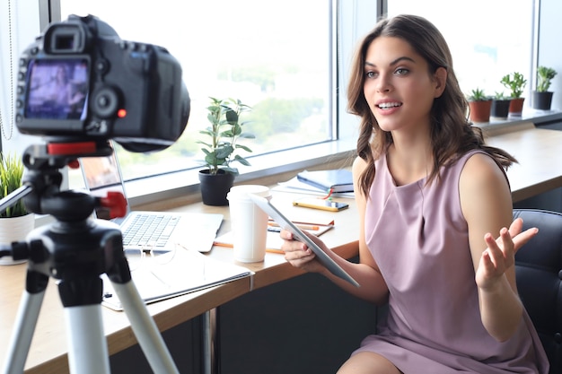 Mulher jovem e bonita conversando e sorrindo enquanto faz um novo vídeo para seu blog.