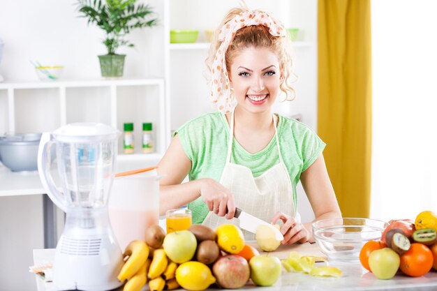 Mulher jovem e bonita cortando a maçã em uma cozinha. Olhando para a câmera.