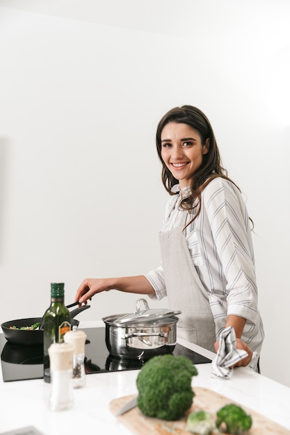 Mulher jovem e bonita cozinhando um jantar saudável em uma panela na cozinha