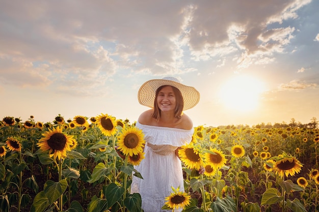 Mulher jovem e bonita curtindo a natureza no campo de girassóis ao pôr do sol