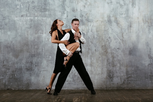 Mulher jovem e bonita de vestido preto e homem dançando tango