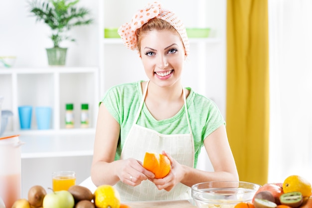 Mulher jovem e bonita descascando laranjas em uma cozinha. Olhando para a câmera.