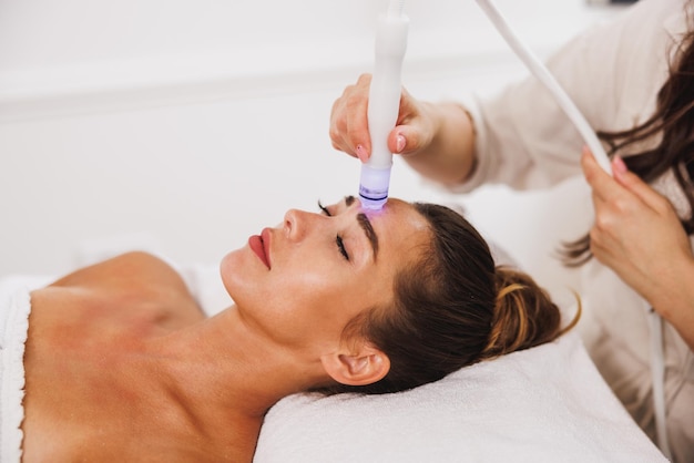 Foto mulher jovem e bonita desfrutando de um tratamento hidrafacial no salão de beleza.