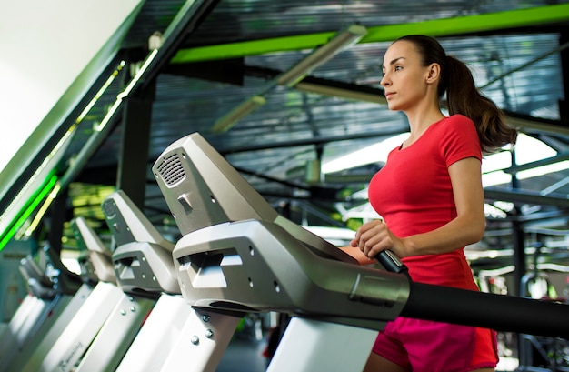 Mulher jovem e bonita desportiva magro em roupas de fitness está correndo na esteira na academia.