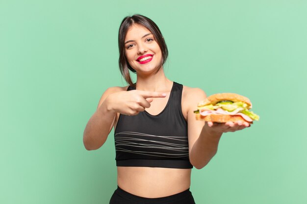 Mulher jovem e bonita do esporte apontando ou mostrando e segurando um sanduíche