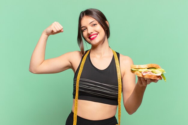 Mulher jovem e bonita do esporte comemorando uma vitória bem-sucedida e segurando um sanduíche