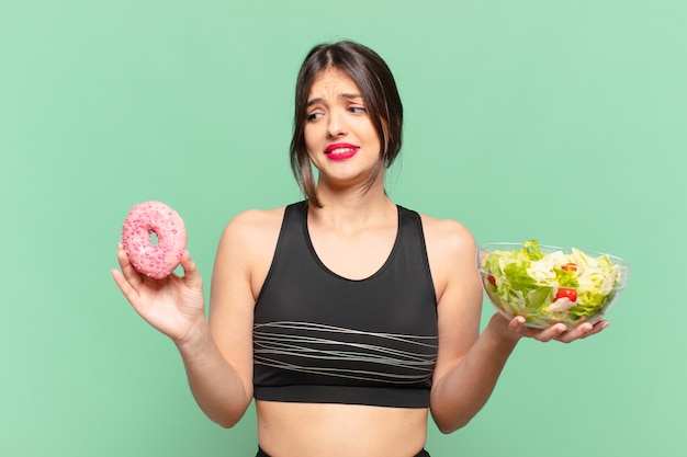 Mulher jovem e bonita do esporte duvidando ou com uma expressão incerta segurando uma salada