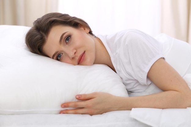 Mulher jovem e bonita dormindo deitada em sua cama e relaxando confortavelmente. É fácil acordar para o trabalho ou para o dia de folga. Conceito de reintegração agradável e de descanso para a vida ativa.