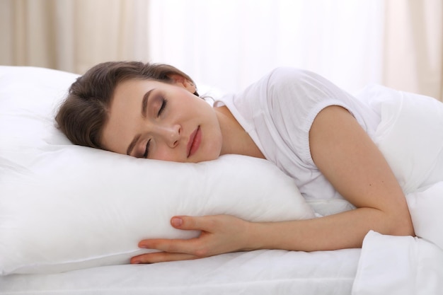 Mulher jovem e bonita dormindo deitada em sua cama e relaxando confortavelmente. É fácil acordar para o trabalho ou para o dia de folga. Conceito de reintegração agradável e de descanso para a vida ativa.