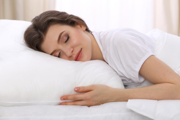 Mulher jovem e bonita dormindo deitada em sua cama e relaxando confortavelmente. É fácil acordar para o trabalho ou para o dia de folga. Conceito de reintegração agradável e de descanso para a vida ativa.