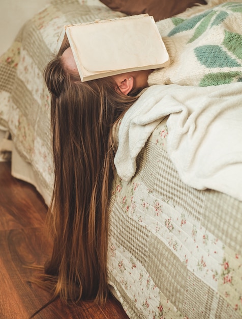 Mulher jovem e bonita dormindo na cama com o livro cobrindo o rosto porque lendo o livro com a preparação do exame da faculdade, mulher com sono com cansaço para que o conceito de lazer, relaxamento e educação.