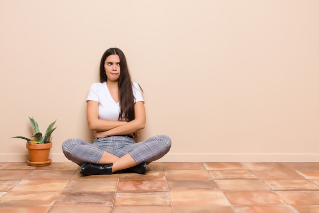 Foto mulher jovem e bonita duvidando ou pensando, mordendo o lábio e sentindo-se insegura e nervosa, procurando copiar o espaço ao lado sentada no chão