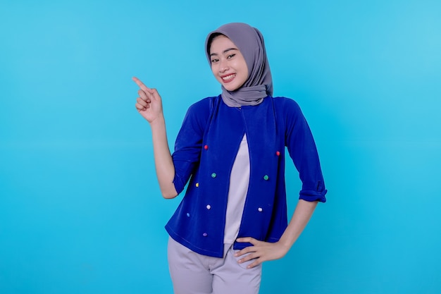 Mulher jovem e bonita e carismática com um hijab apontando isolado em um fundo azul claro