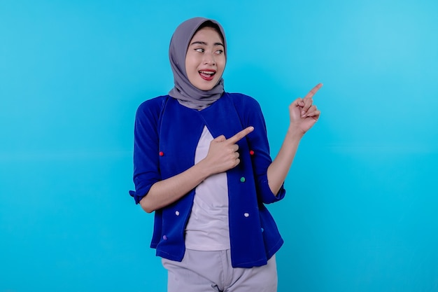 Mulher jovem e bonita e carismática com um hijab apontando isolado em um fundo azul claro