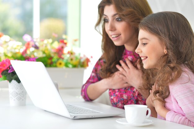 Foto mulher jovem e bonita e menina sentada à mesa e usando laptop