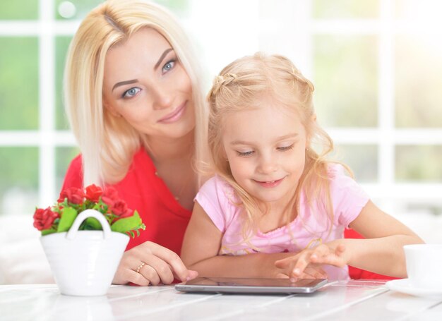 Mulher jovem e bonita e menina sentada à mesa e usando tablet