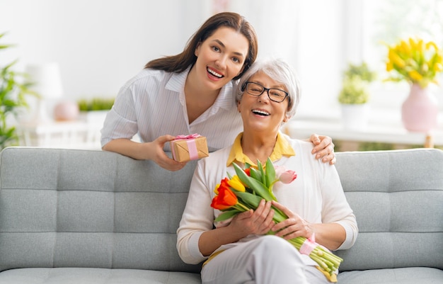 Mulher jovem e bonita e sua mãe com tulipas de flores nas mãos em casa.