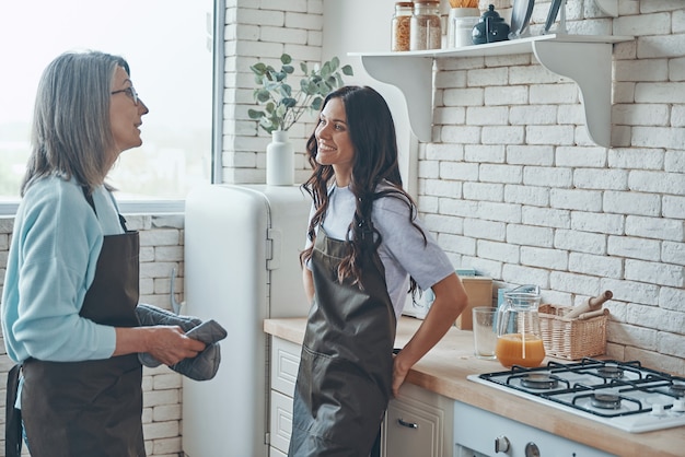 Mulher jovem e bonita e sua mãe se comunicando enquanto passam o tempo na cozinha doméstica