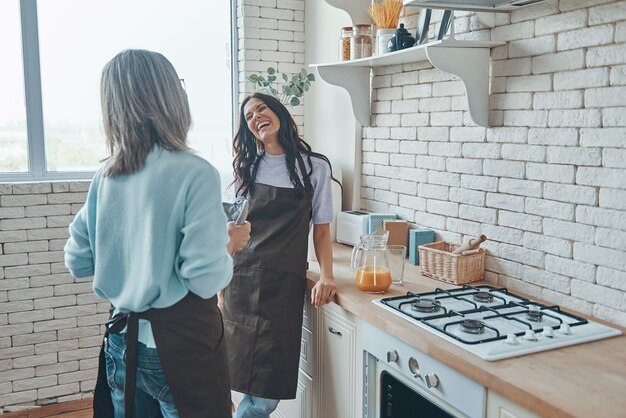 Mulher jovem e bonita e sua mãe se comunicando enquanto passam o tempo na cozinha doméstica