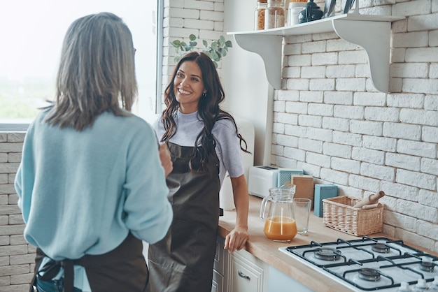 Mulher jovem e bonita e sua mãe se comunicando enquanto passam o tempo na cozinha doméstica