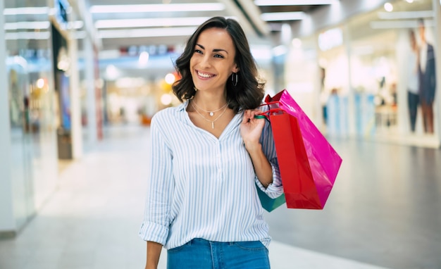 Mulher jovem e bonita elegante com sacolas de compras andando no shopping