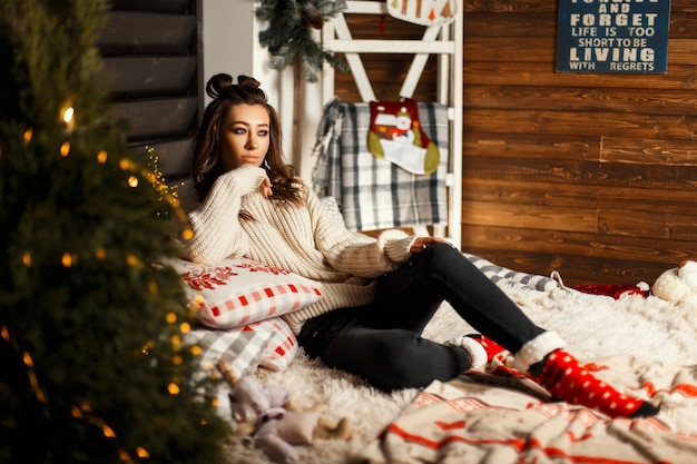 Mulher jovem e bonita elegante em um suéter vintage de tricô com meias vermelhas de Natal deitada na cama