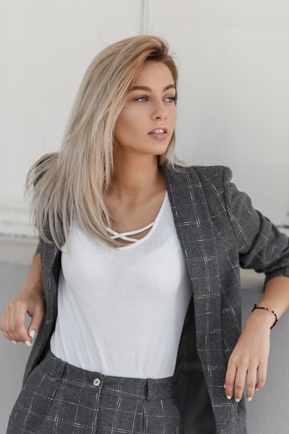 Mulher jovem e bonita elegante modelo loira em um terno vintage cinza da moda com camiseta branca posando na rua