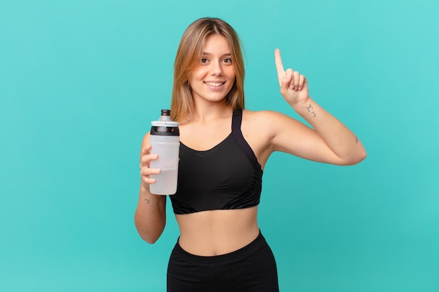 Mulher jovem e bonita em boa forma, sorrindo e parecendo amigável, mostrando o número um