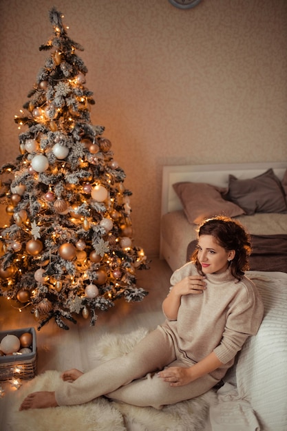 Mulher jovem e bonita em casa no quarto perto da árvore de natal.