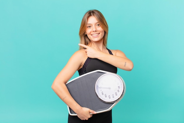 Mulher jovem e bonita em fitness sorrindo alegremente, sentindo-se feliz e apontando para o lado