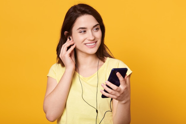 Mulher jovem e bonita em fones de ouvido, ouvindo música através de seu telefone móvel moderno