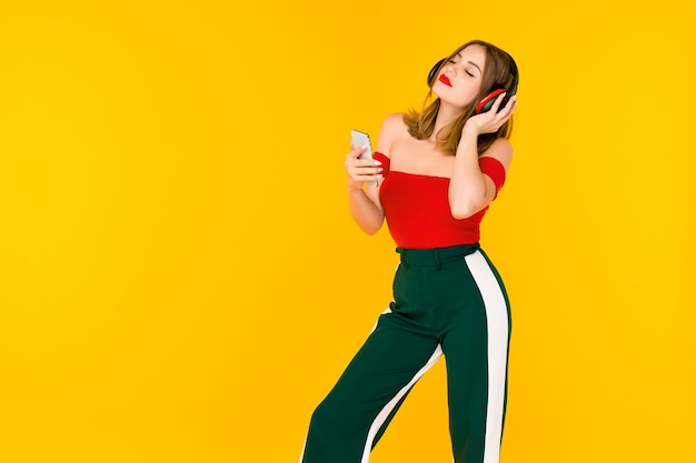 Mulher jovem e bonita em fones de ouvido, ouvindo música em fundo amarelo - imagem