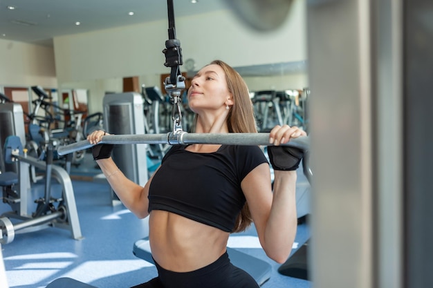 Mulher jovem e bonita em forma, exercitando-se em uma máquina de puxar para baixo na academia