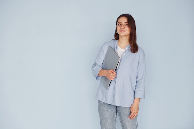 Mulher jovem e bonita em jeans e camisa azul em pé contra a parede com o laptop nas mãos