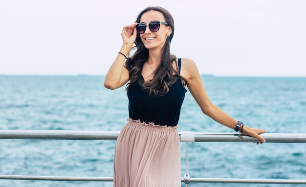 Mulher jovem e bonita em óculos de sol e vestido em barco de cruzeiro de luxo. Mulher de férias de navio de cruzeiro, aproveitando a viagem no mar. Mulher livre e feliz olhando para o oceano