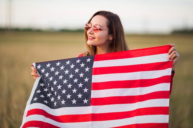 Mulher jovem e bonita em óculos de sol rosa com bandeira americana