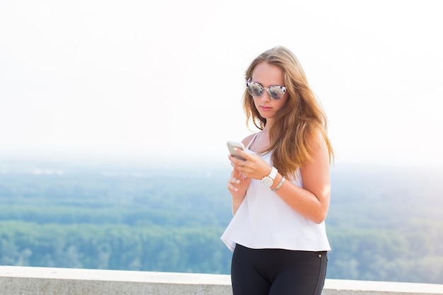 Mulher jovem e bonita em óculos de sol usa smartphone na natureza