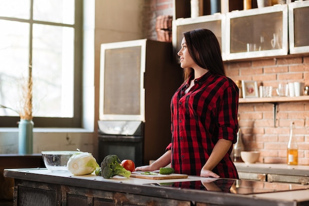 Foto mulher jovem e bonita em pé à mesa na cozinha e desviar o olhar.