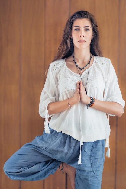 Mulher jovem e bonita em pé em uma pose de árvore de iogaVrikshasana com as mãos em posição de oração