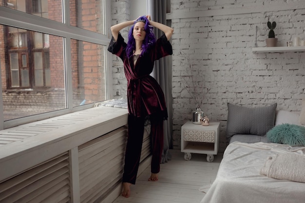 Foto mulher jovem e bonita em pijama roxo escuro de veludo chique posando em seu quarto