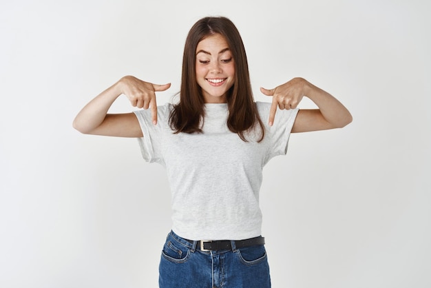 Mulher jovem e bonita em roupas casuais apontando e olhando para o banner promocional mostrando propaganda em fundo branco