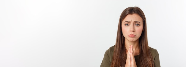 Mulher jovem e bonita em roupas casuais juntos de mãos dadas e rezando isolado no branco