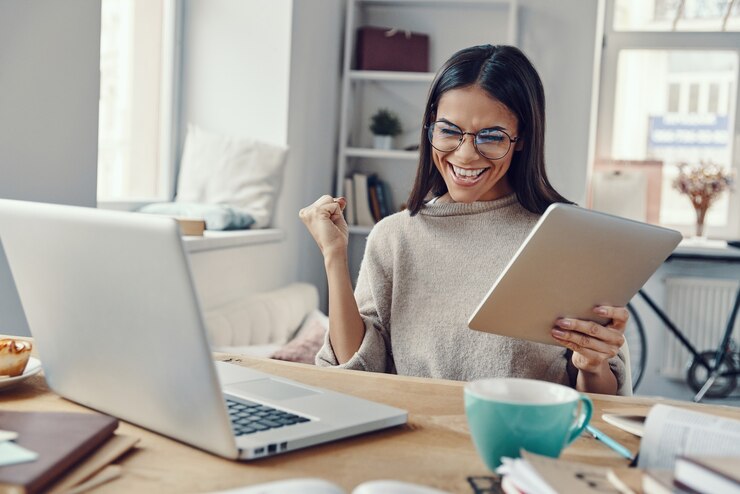 Foto mulher jovem e bonita em roupas casuais usando laptop e torcendo enquanto trabalha dentro de casa