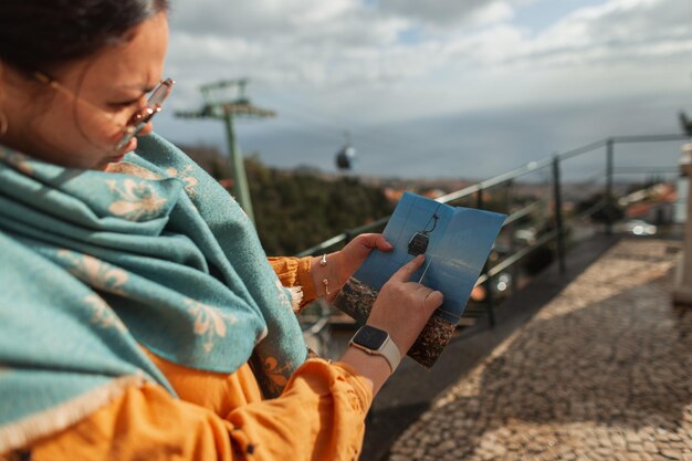 Mulher jovem e bonita em roupas de moda primavera com um cachecol e óculos de sol está segurando um mapa e apontando o dedo Menina bonita viajando na ilha da Madeira Portugal