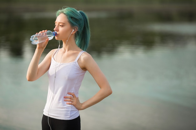 Mulher jovem e bonita em roupas esportivas fazendo ioga perto do lago