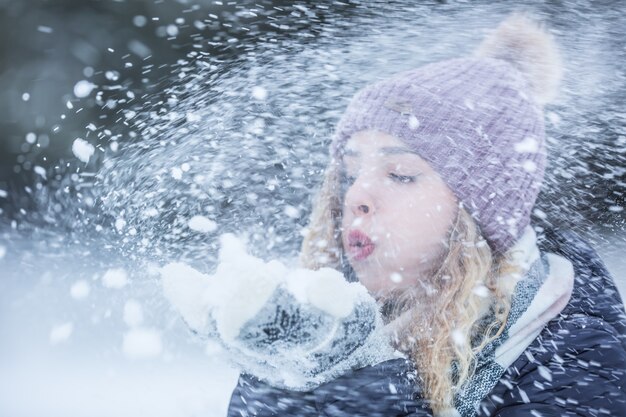 Mulher jovem e bonita em roupas quentes, soprando de neve.