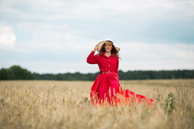 Mulher jovem e bonita em roupas vermelhas com um chapéu atravessa o campo no verão