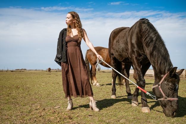 Mulher jovem e bonita em um campo com cavalos. Modelo de moda atraente.