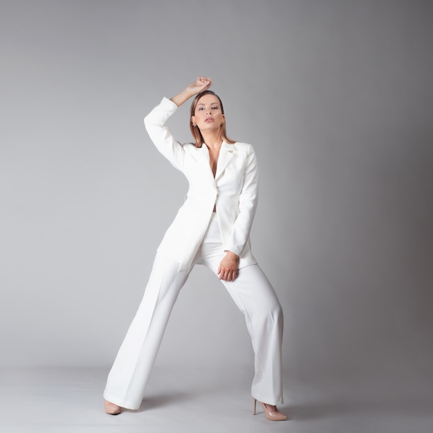 Mulher jovem e bonita em um terno branco da moda em uma pose dinâmica