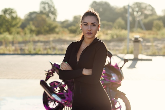Mulher jovem e bonita em um terno preto apertado poses perto de motocicleta esporte em carro self-service